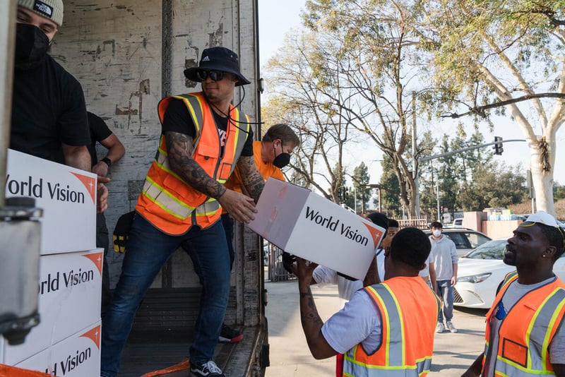 Men wearing orange vests pass white boxes to each other to move them off of a truck.