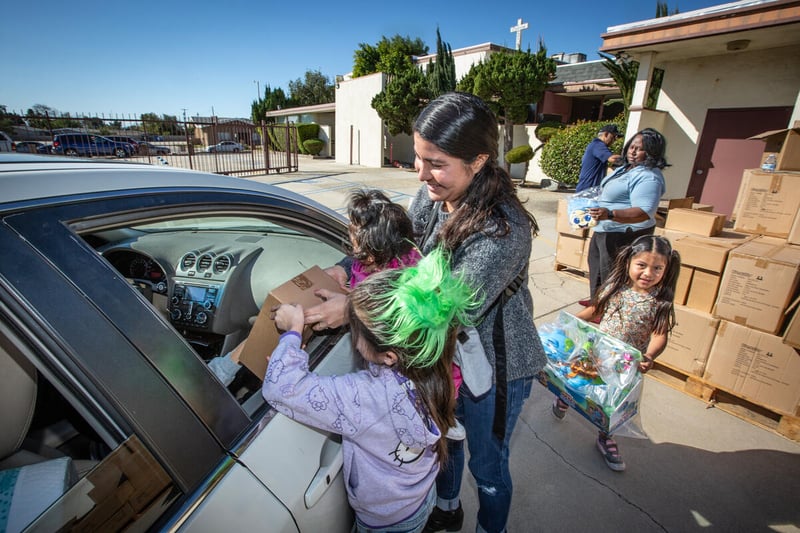 A mother and three young girls hand a box through a car window.