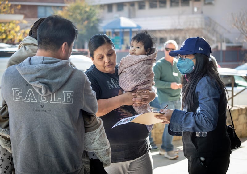 A woman holds some papers while talking to a woman holding a baby and a man holding a child.