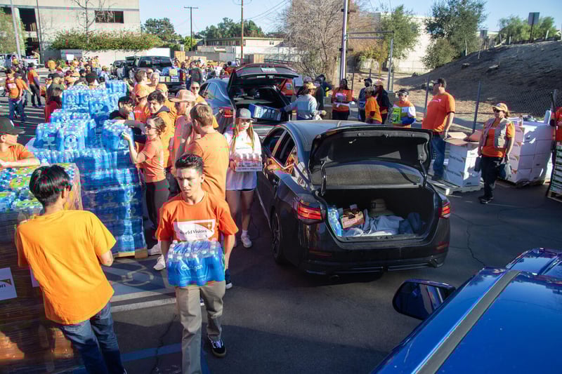 Volunteers carry boxes and cases of water to load in cars as they drive through a distribution.
