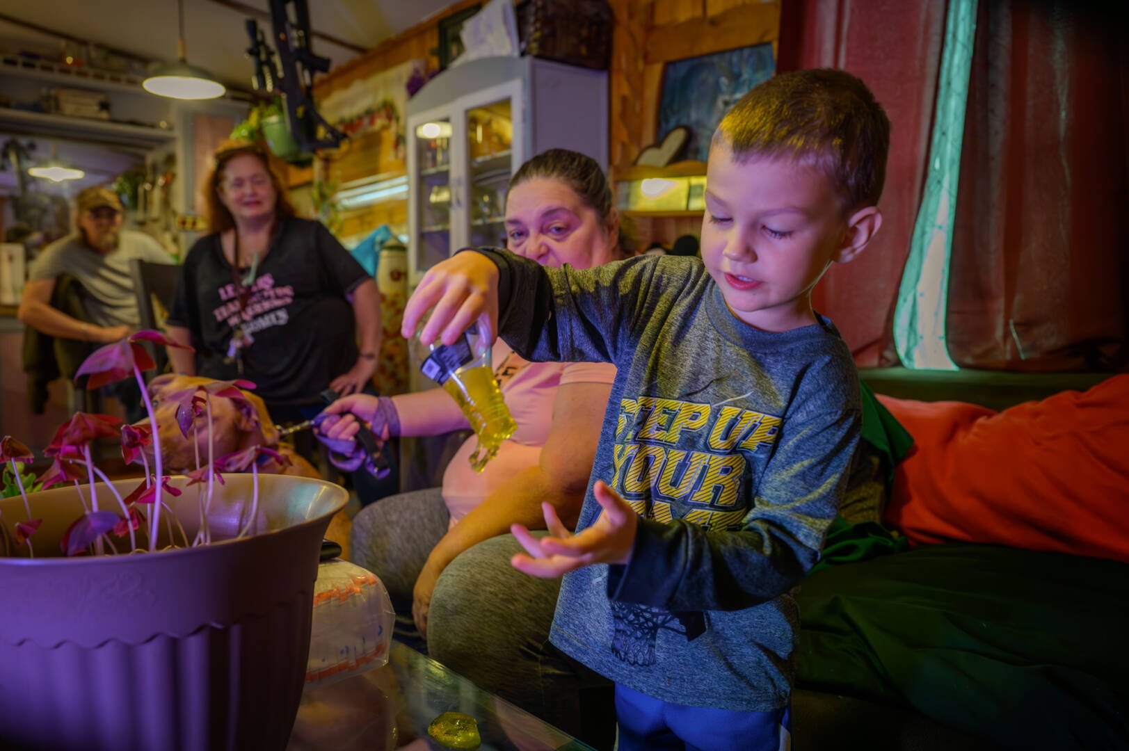 A little boy plays with a bottle of toy slime while three adults look on in the background.