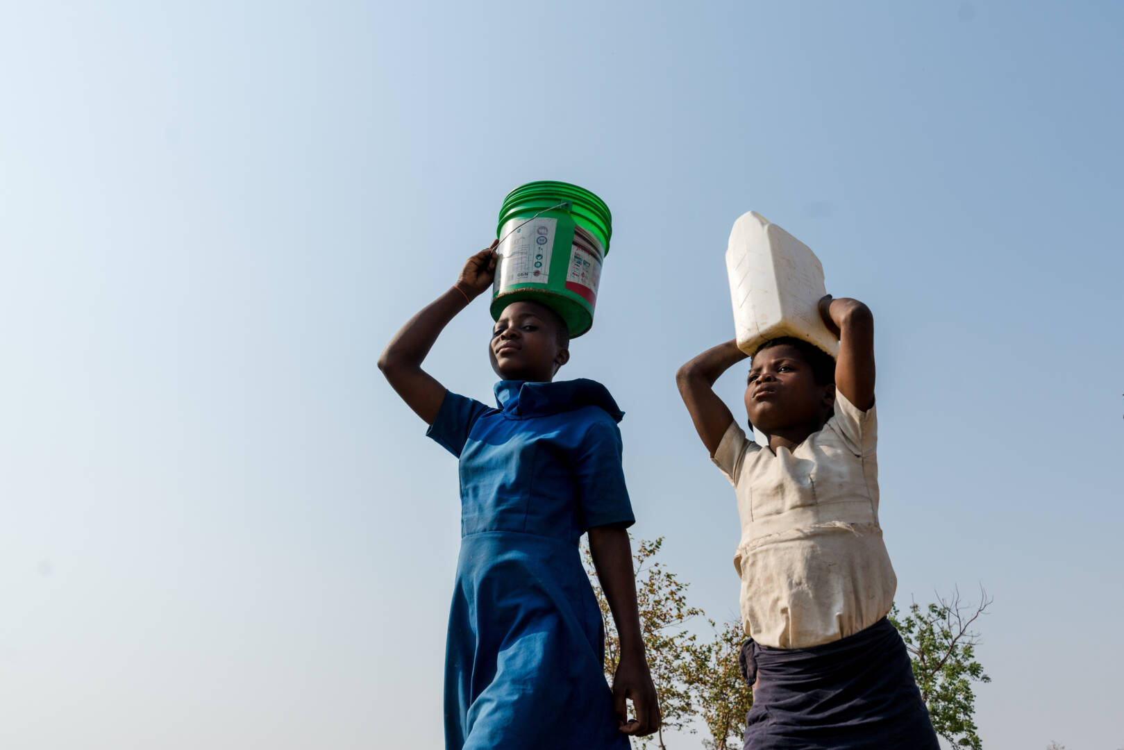 A close-up view of two girls carrying containers on their heads.