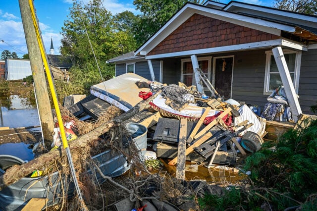 Debris piled near a damaged doorstep of a home on a sunny day.