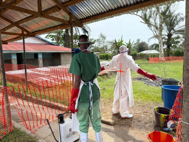 A health worker disinfects a man covered in protective gear.