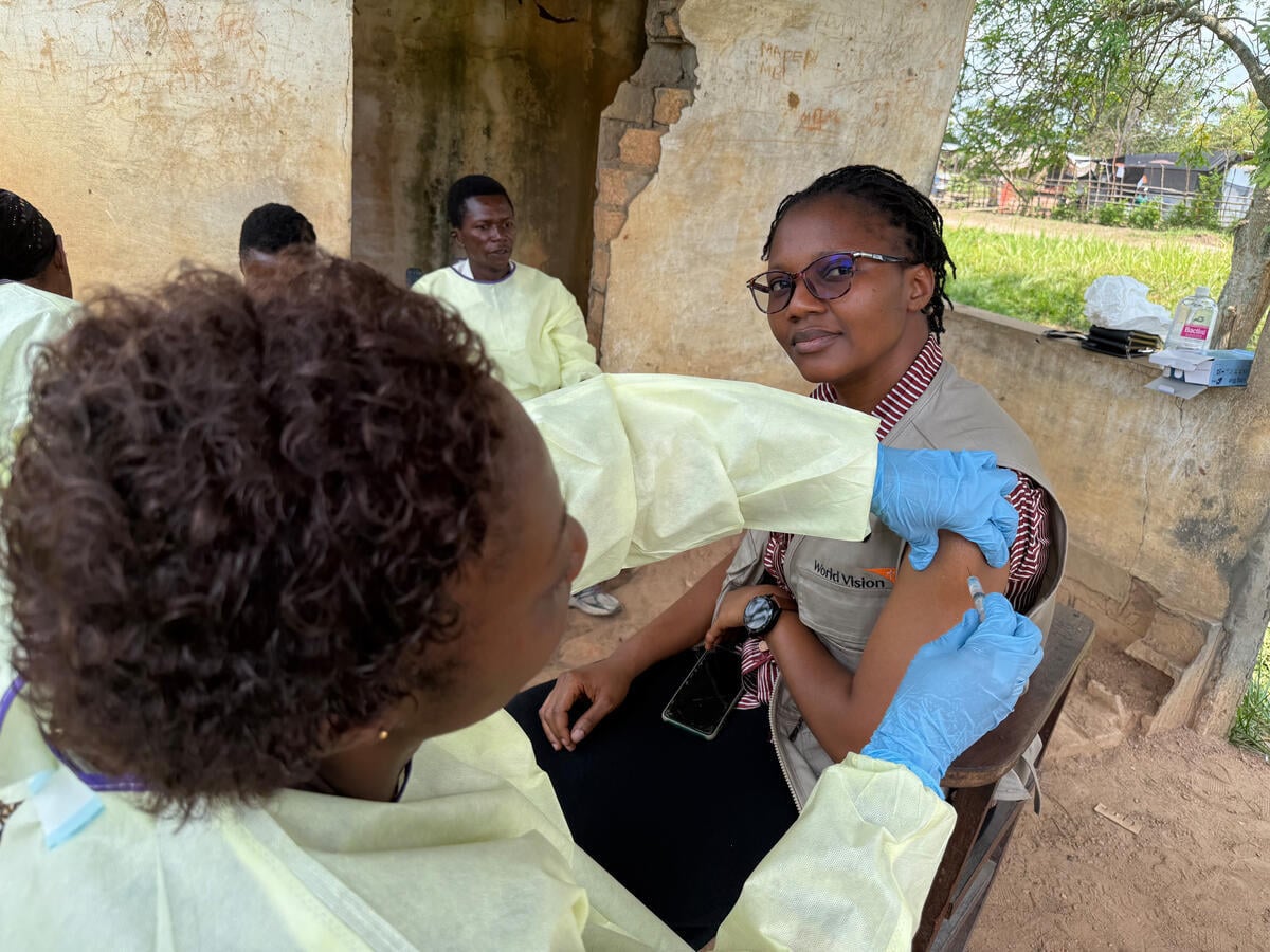 A health worker administers a shot into the arm of a woman who is looking at the camera.