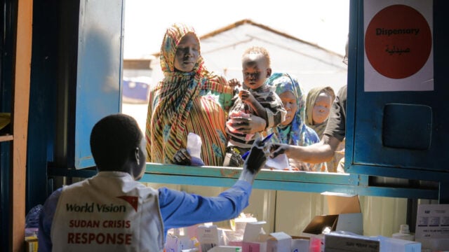 Sudanese refugees line up at a window where a health worker is handing out supplies.