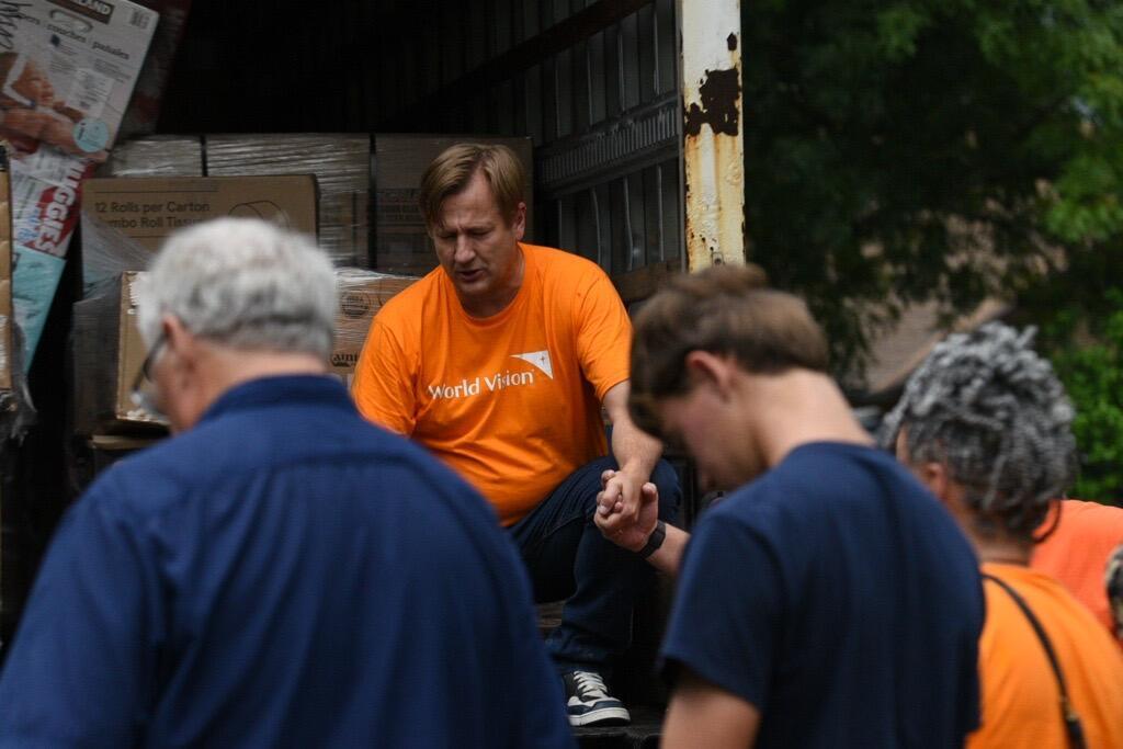 People hold hands in a moment of prayer at a humanitarian aid distribution site.