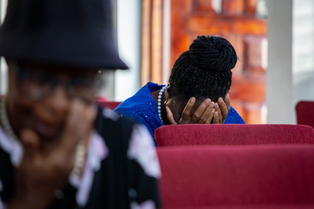 One woman sits with her head in her hands, while another person in another row ahead wipes away a tear.