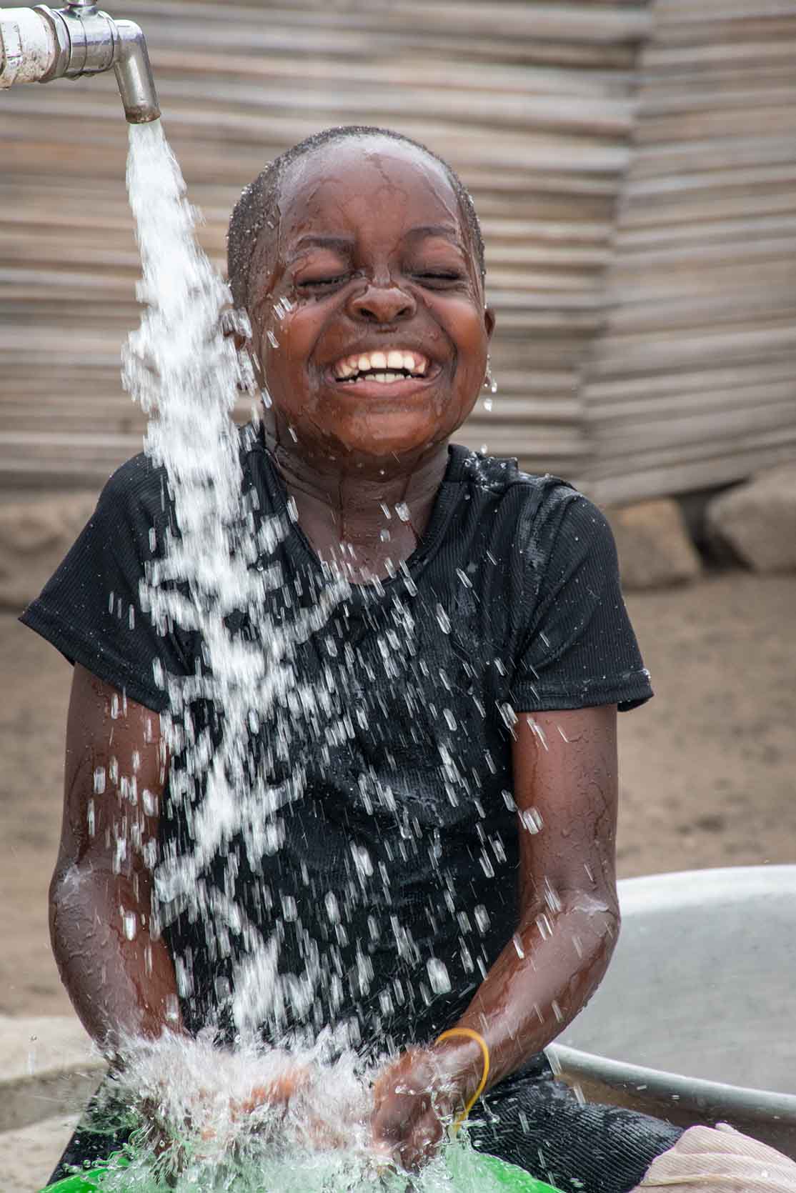 A young girl closes her eyes and smiles while water splashes into her bucket.