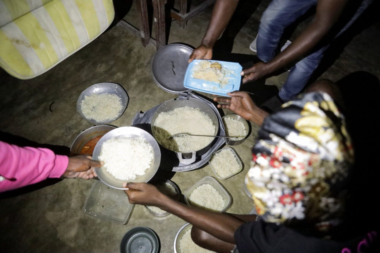 People hold plates of rice inside a shelter in Haiti. Containers with rice rest on the floor.