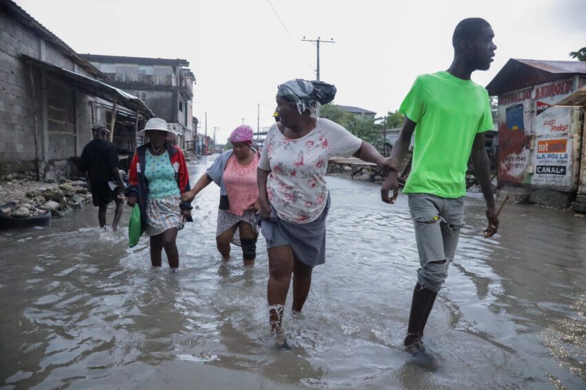 A group of people wade hand in hand through a flooded street in Haiti.