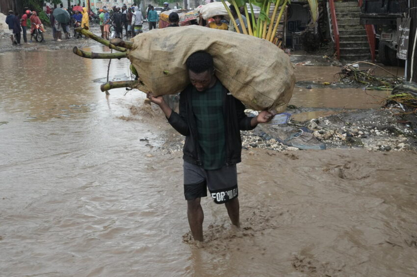 A man carries a large bag over his shoulders. Water comes up above his ankles.