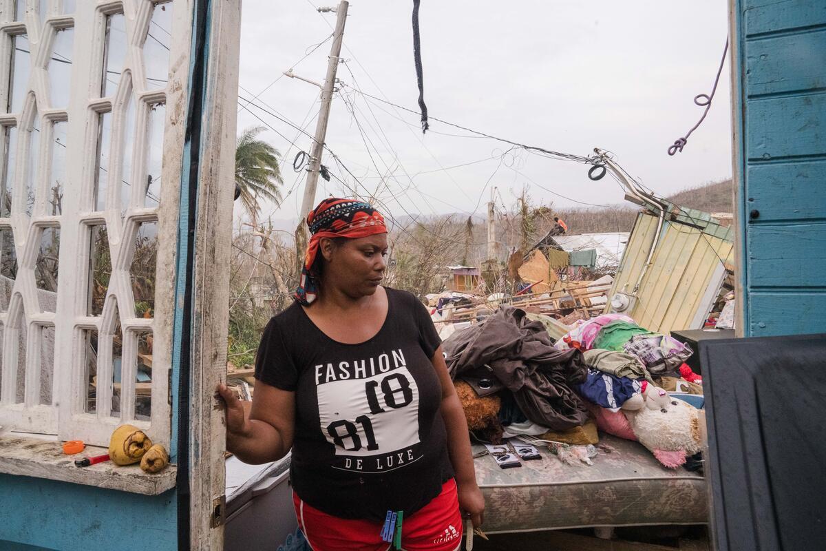 A woman glances away while standing in the doorway of her storm-damaged home. 
