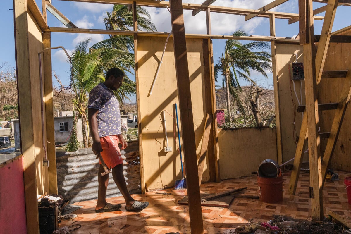 A man holding a hammer stands among the wreckage of his home.