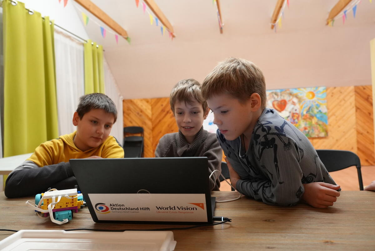 Three boys gather around a computer in a bright and cheerful room.
