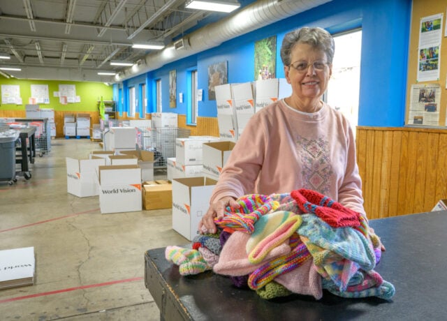 Portrait of a woman in a warehouse. On the table in front of her is a pile of knit caps.
