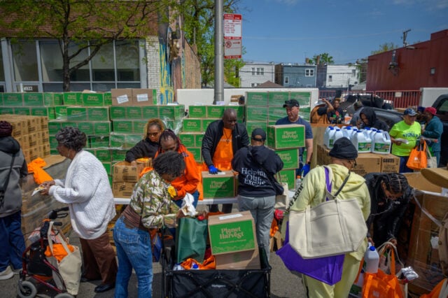 People pushing carts walk past a table stacked high with boxes.