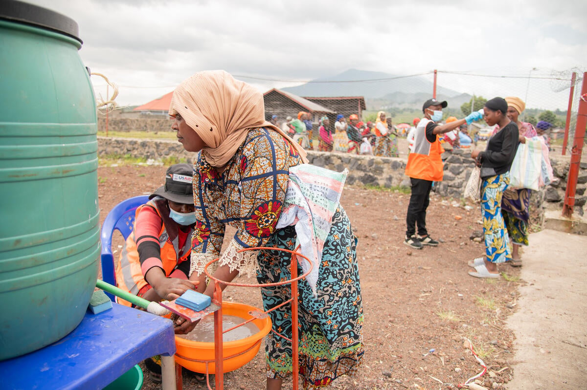 A woman washes her hands over a plastic basin as aid workers assist people lined up at a handwashing station to prevent the spread of Ebola. 