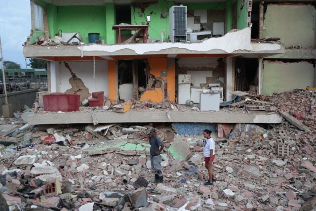 A woman stands amid the ruins of a toppled building impacted by twin earthquakes.