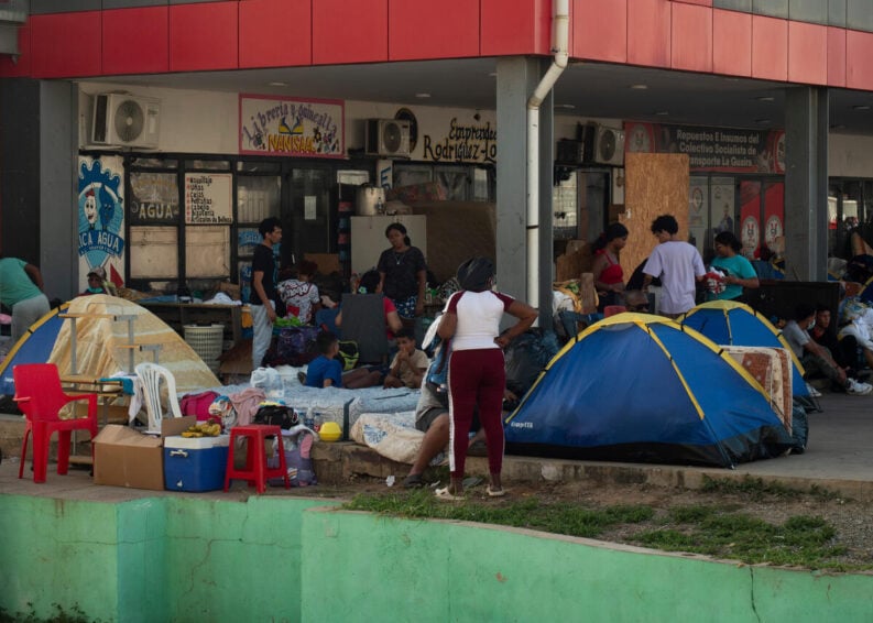 People gather outside businesses with tents and plastic chairs set up underneath a building.