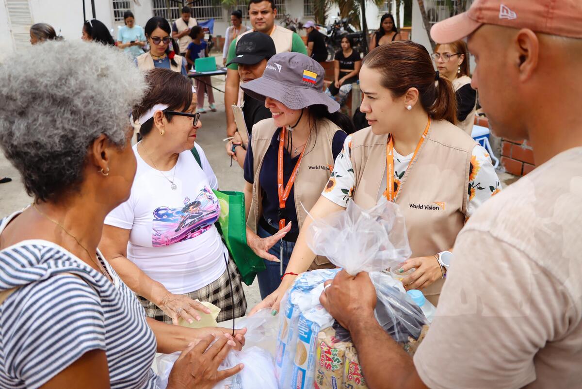 Female aid workers wearing World Vision-branded vests connect with earthquake survivors during an outdoor relief distribution.