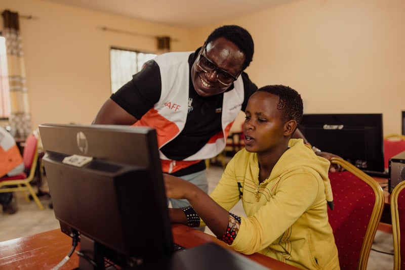 A woman points to a computer screen while a man stands beside her looking at what she is pointing at.