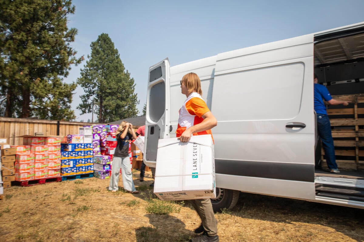 A World Vision aid worker carries boxes of relief supplies from a vehicle to a distribution site serving people affected by wildfires.