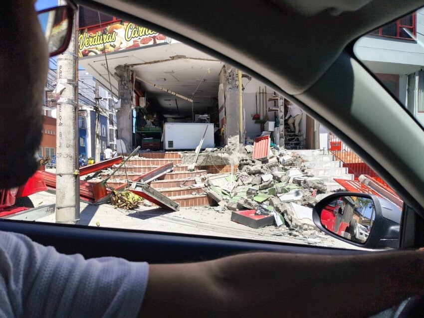 A motorist looks out a car window at a damaged building and debris after an earthquake.