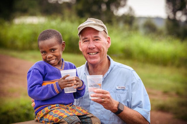 A man and a girl each hold a cup of water while looking at the camera smiling.