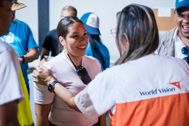 A woman with a radio clipped to her shirt smiles as an aid worker rests a hand on her shoulder during a meeting.