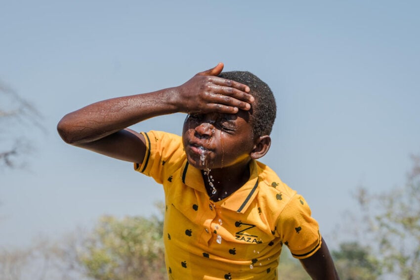 A young girl splashes water on her face under the bright sun in Malawi.