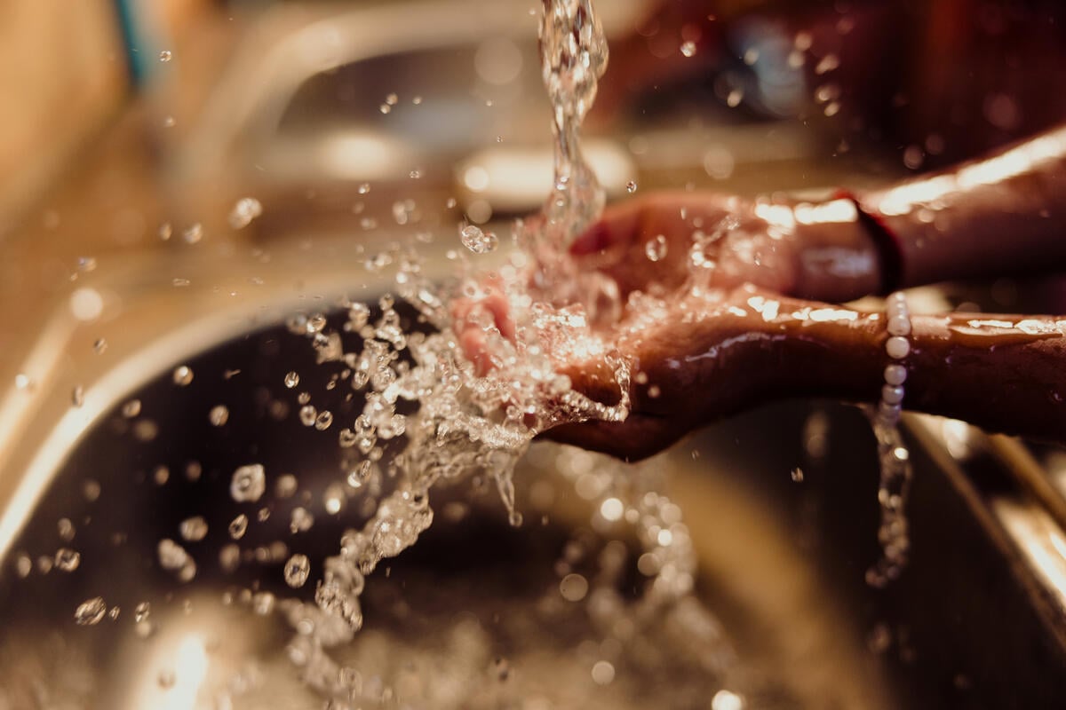 Water flows over the open hands of a child wearing bracelets at a sink.