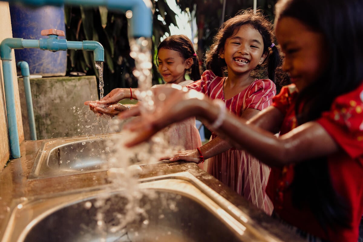 Three girls laugh as they wash their hands at a handwashing station.