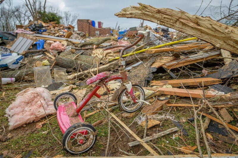 A bent and dirty red tricycle rests among an extensive pile of debris.