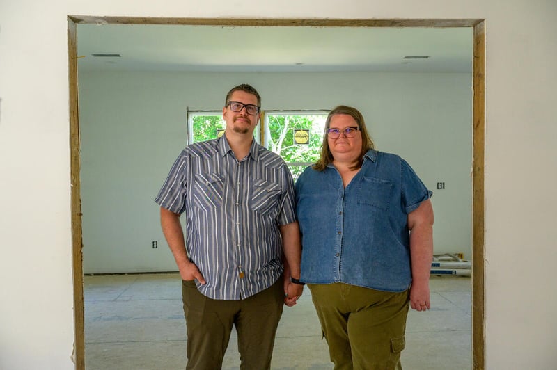 A man and woman hold hands as they stand in the doorway of their rebuilt home.