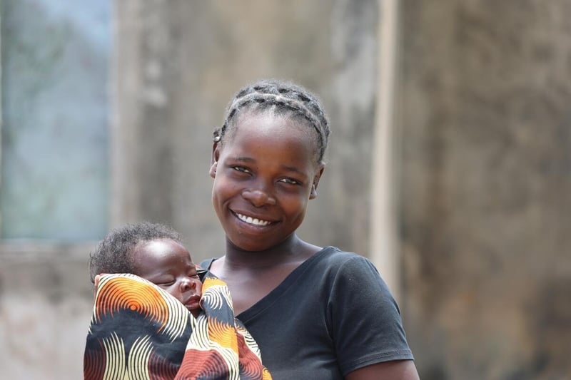 A woman holds her sleeping baby and smiles with joy.