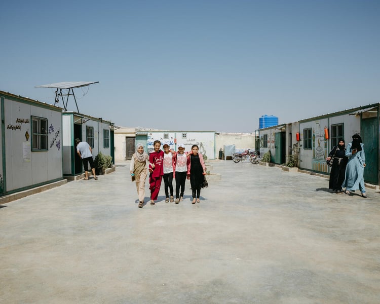 Children walk on cement. Around them are informal homes.