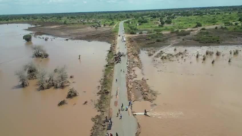 Aerial view of roadway amid floodwaters with people walking on the roadway and a car.
