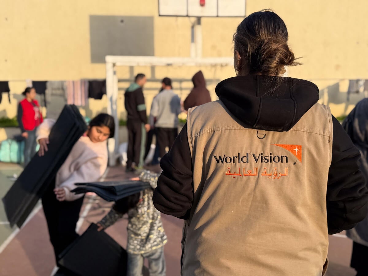 A World Vision aid worker stands near a group of people gathered on a playground as people stand and gather to receive assistance.