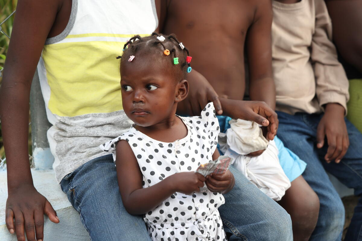 A child with braids wearing a polka-dot shirt holds a packet of therapeutic food while leaning against an older child.
