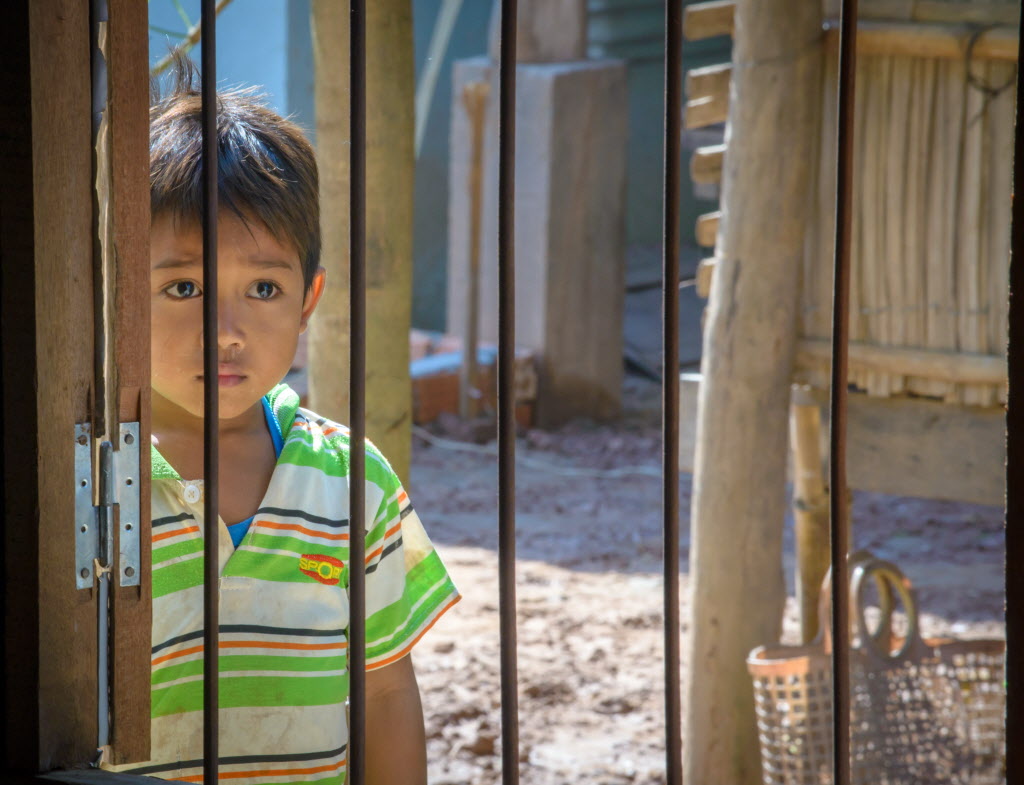 Boy looks through bars in World Vision project area in Cambodia. Photo ©2015 Laura Reinhardt | World Vision.
