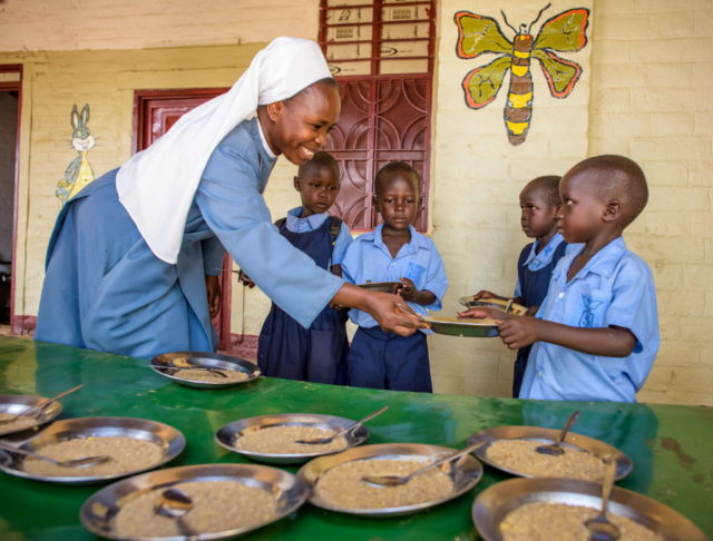 Sister Margaret hands out bowls of food to children at St. Joseph School in Kuajok, one of many 